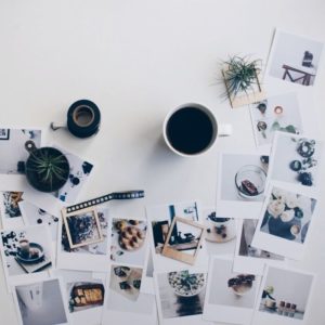 Faded Polaroid photos scattered on white desk with coffee cup and plants, creative workspace for photography and design.