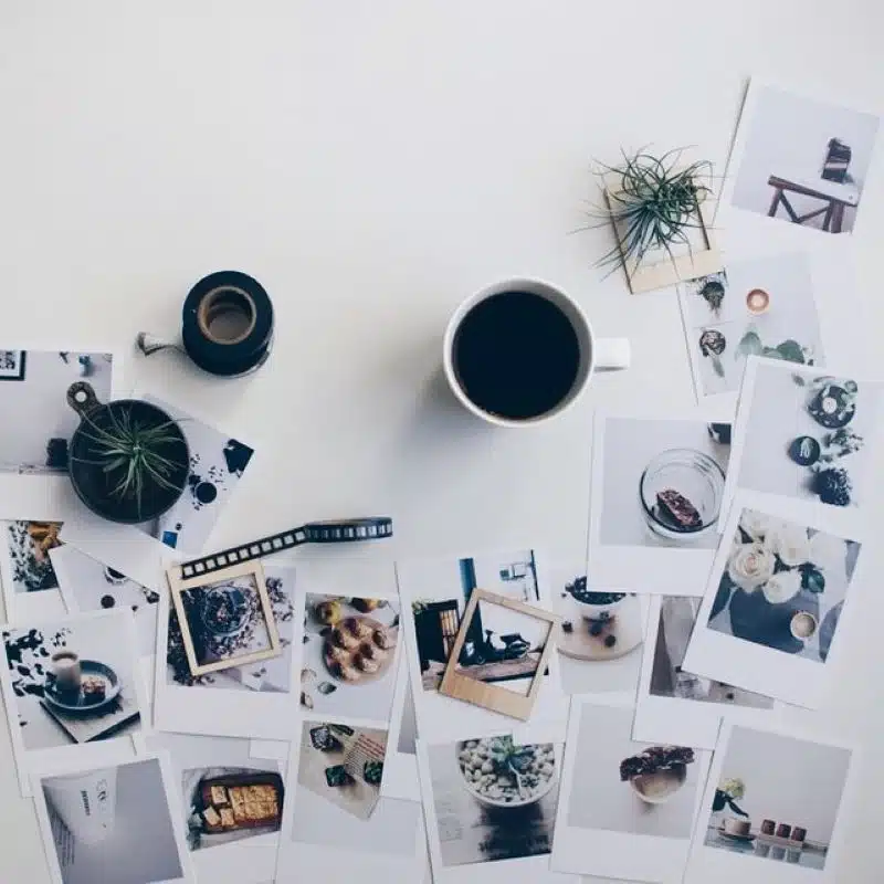 Faded Polaroid photos scattered on white desk with coffee cup and plants, creative workspace for photography and design.
