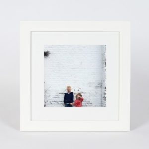 Children smiling in front of a white brick wall framed photo, perfect for wall art decor.
