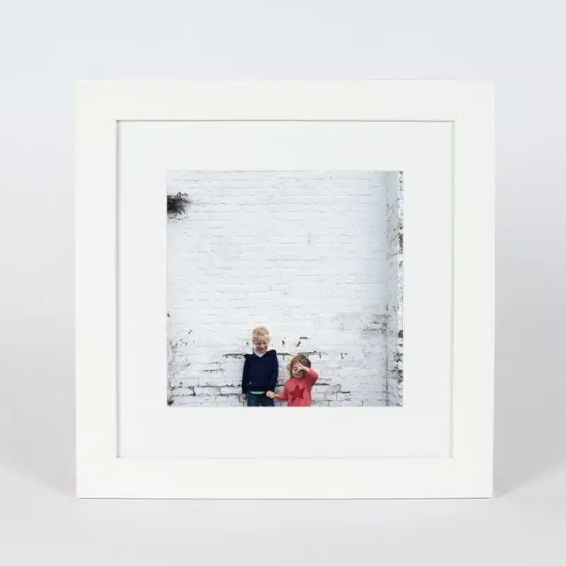 Children smiling in front of a white brick wall framed photo, perfect for wall art decor.