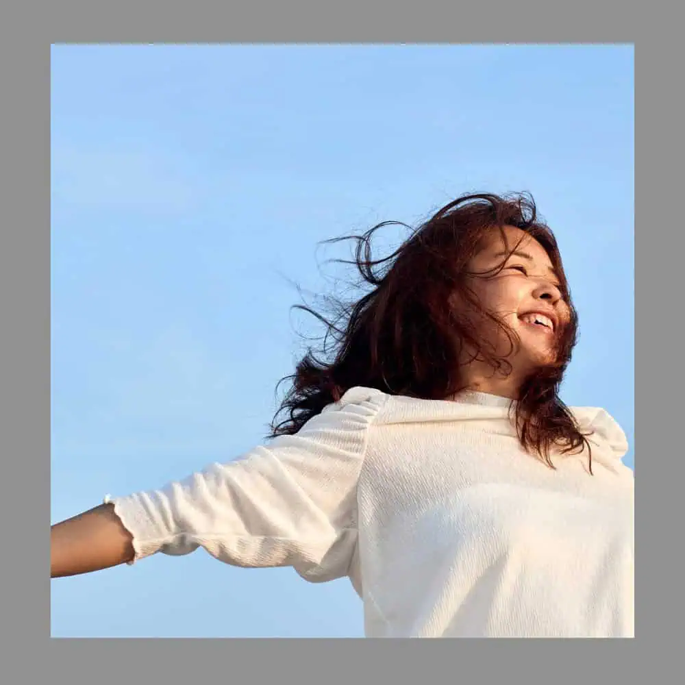 Free-spirited woman enjoying outdoor breeze and sunlight, symbolising freedom and happiness.